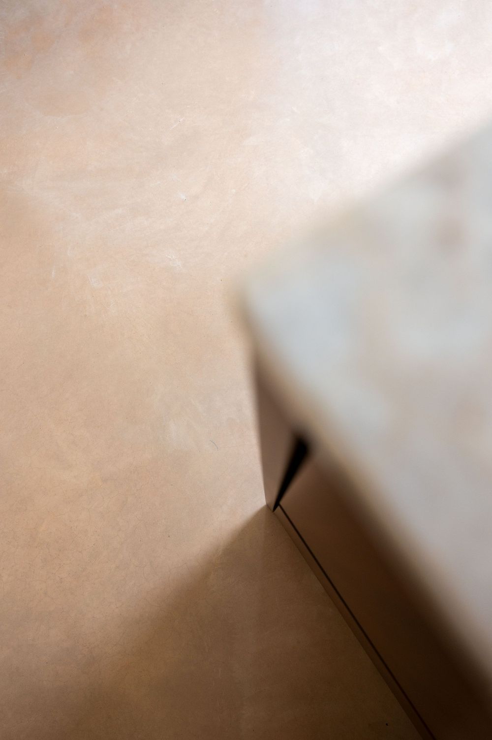 Close-up abstract view of a cardboard box corner against a beige textured wall surface.