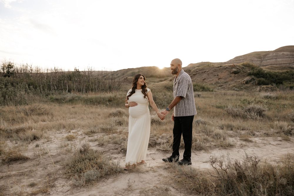 Pregnant couple holds hands in golden hour light amid Albertas landscape during their maternity photoshoot
