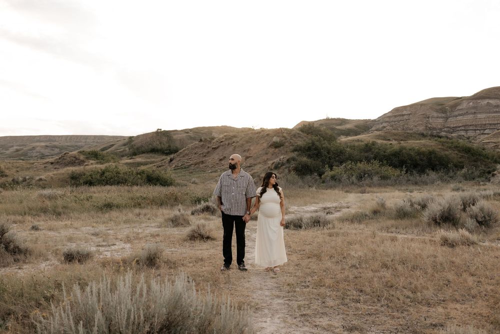 Couple holding hands on a dirt path in a vast badlands landscape with rolling hills and dry grasslands.