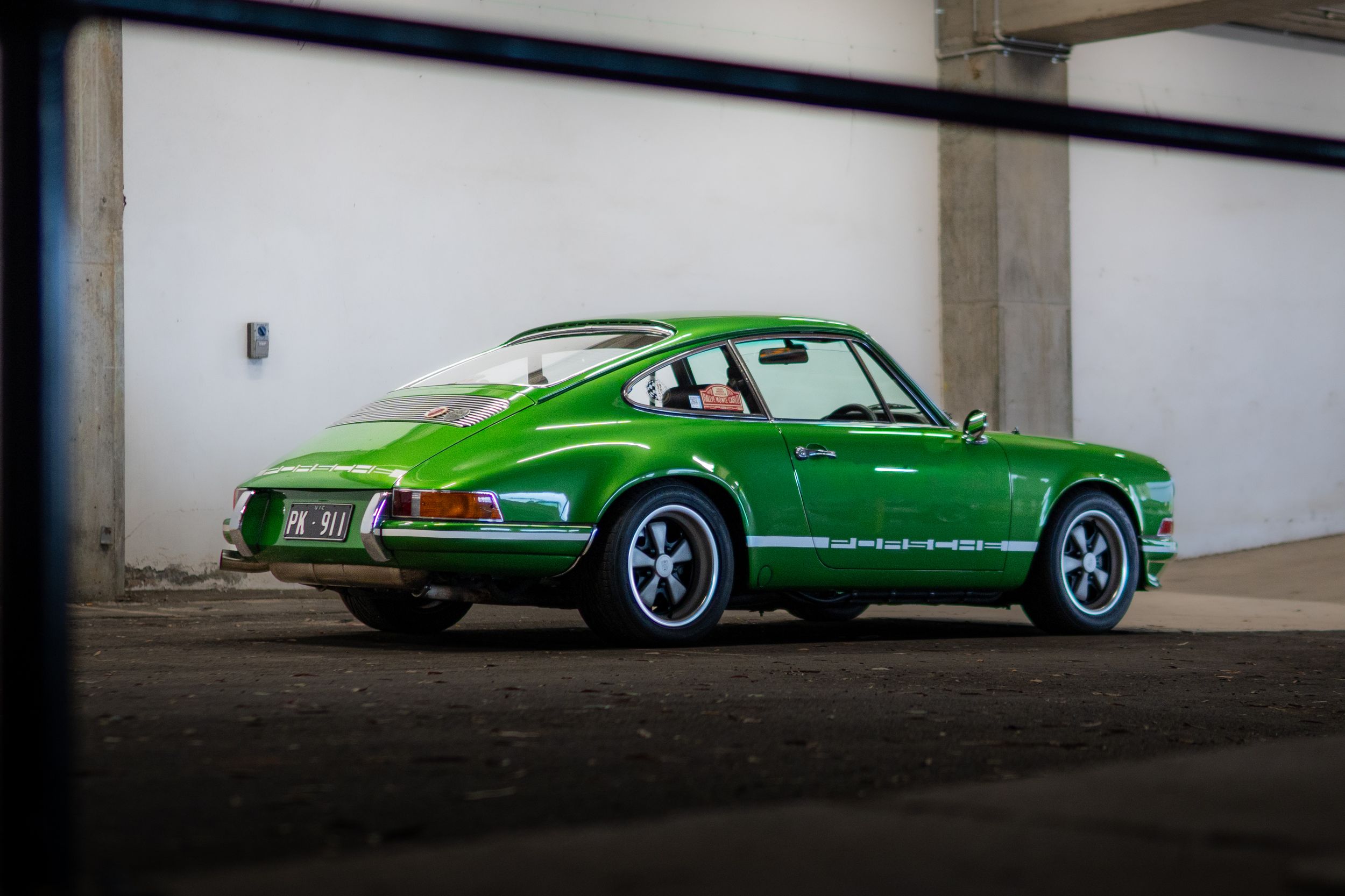 Classic green Porsche 911 RS parked in industrial setting, rear three-quarter view.