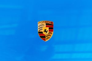 Close-up of Porsche crest badge logo on a vibrant blue car hood surface.