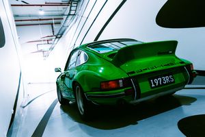 Rare green Porsche 911 RS 1973 parked in a bright white corridor, rear spoiler visible.