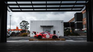 Red Porsche 935 race car number 23 parked under building overhang on overcast day.