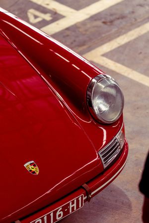 Detail shot of vintage red Porsche 356 front hood with round headlight and chrome trim.