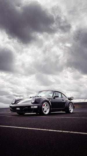Classic black Porsche 911 Turbo parked on open road under dramatic cloudy grey sky.