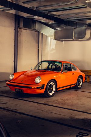 Classic orange Porsche 911 in a parking garage, side-front angle highlighting iconic retro styling.
