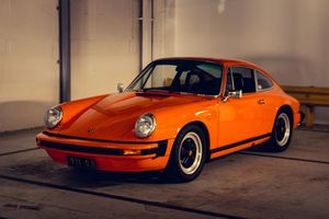 Vintage orange Porsche 911 parked in a garage, front three-quarter view showcasing classic design.
