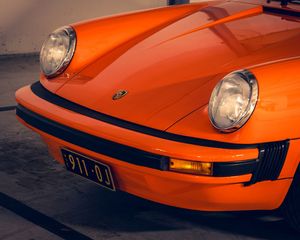 Close-up front view of a classic orange Porsche 911 with round headlights and vintage license plate.