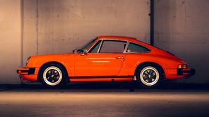 Side profile of a classic orange Porsche 911 with white trim wheels against a neutral background.
