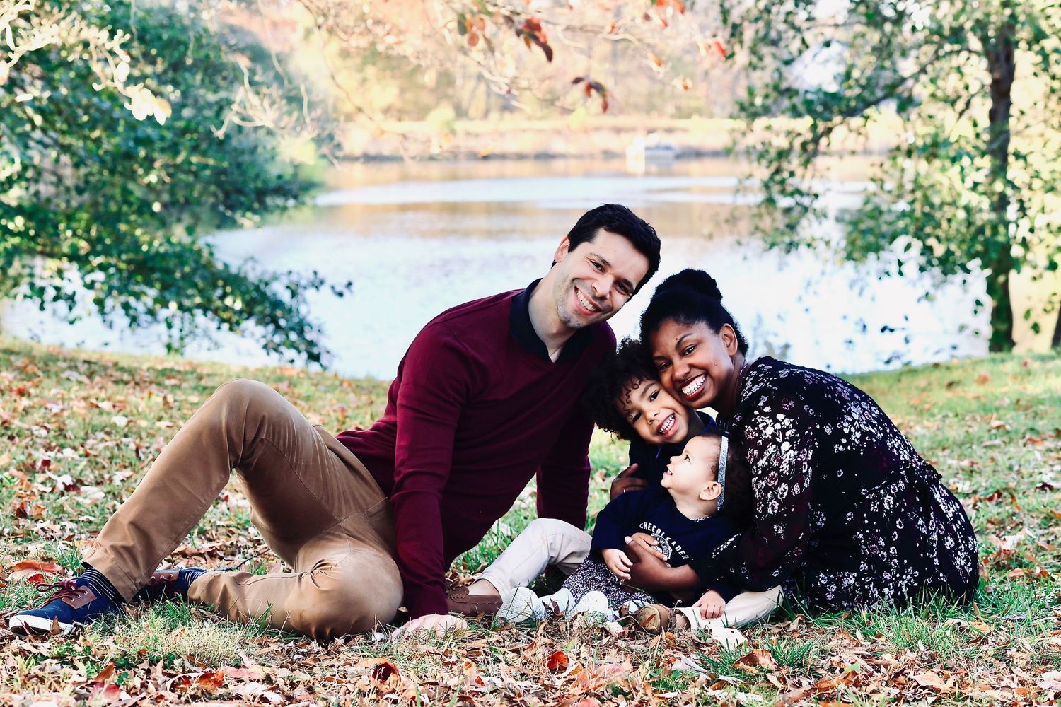 Smiling family sitting on autumn leaves near a lake.