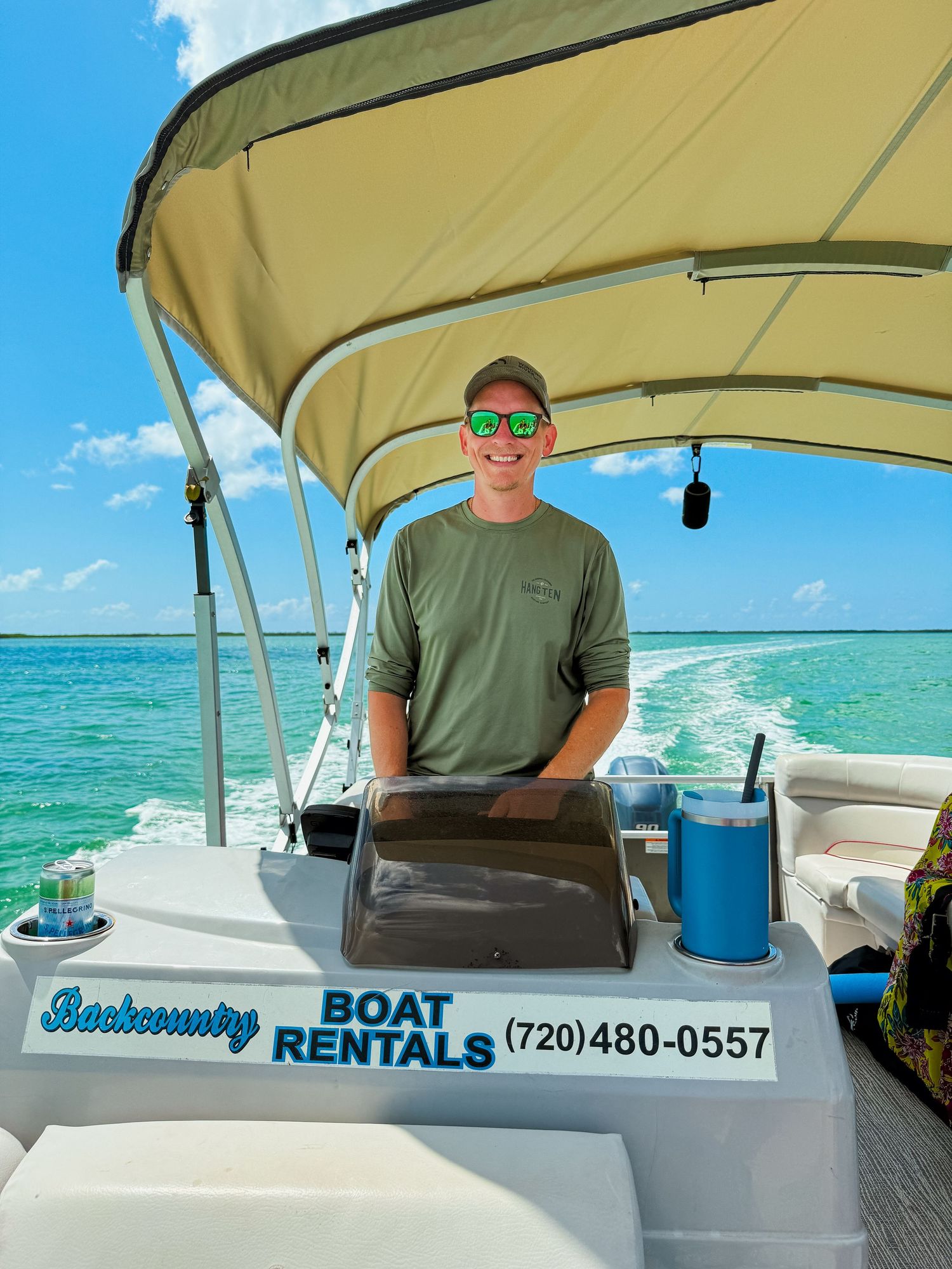 Smiling man steering Backcountry Boat Rentals pontoon on turquoise Florida waters.