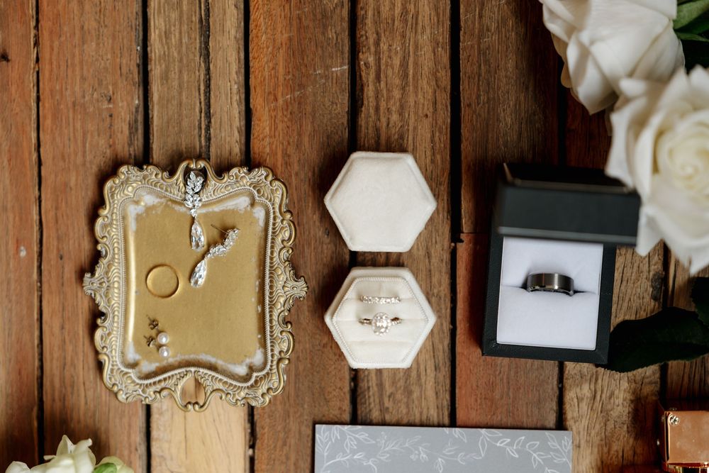 Wedding rings in hexagon velvet box, jewelry on ornate gold tray, and black ring box on rustic wood surface.  Clifton Woolshed