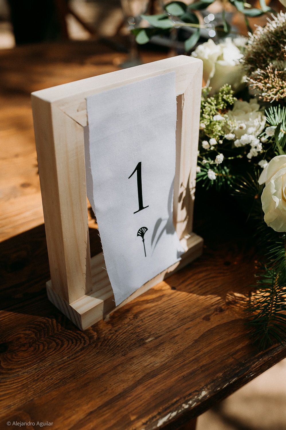 Rustic wooden table number holder displaying number 1 on elegant card, surrounded by white floral wedding centerpiece.