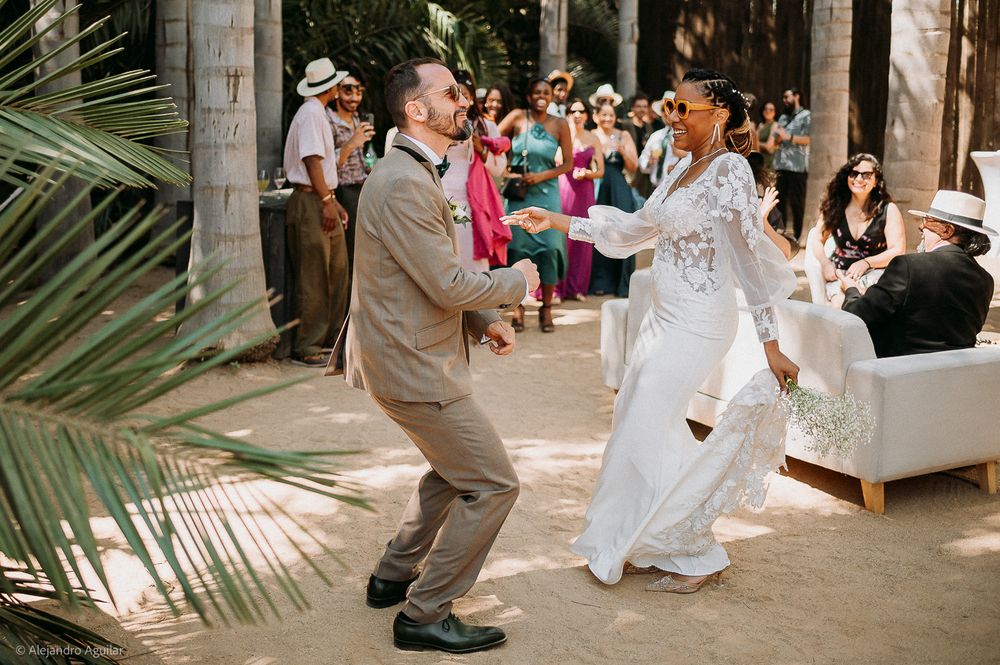 Bride and groom share a joyful first dance outdoors at a tropical wedding venue surrounded by guests.
