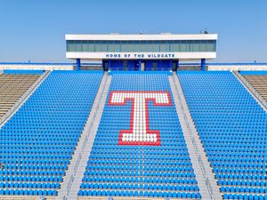 Empty blue stadium seats with a red and white T logo, Home of the Wildcats press box under clear blue sky.