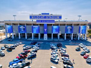 Aerial view of Wildcat Stadium exterior with blue banners, surrounded by a busy parking lot on a sunny day.