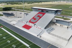 Aerial view of a high school football stadium with red and white bleachers and large letter S logo on the stands.