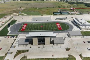 Aerial view of a high school football stadium with red turf field, running track, and modern facilities in a suburban setting.