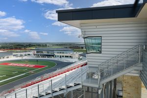 Aerial view of a high school stadium press box overlooking a red turf football field and track on a sunny day.