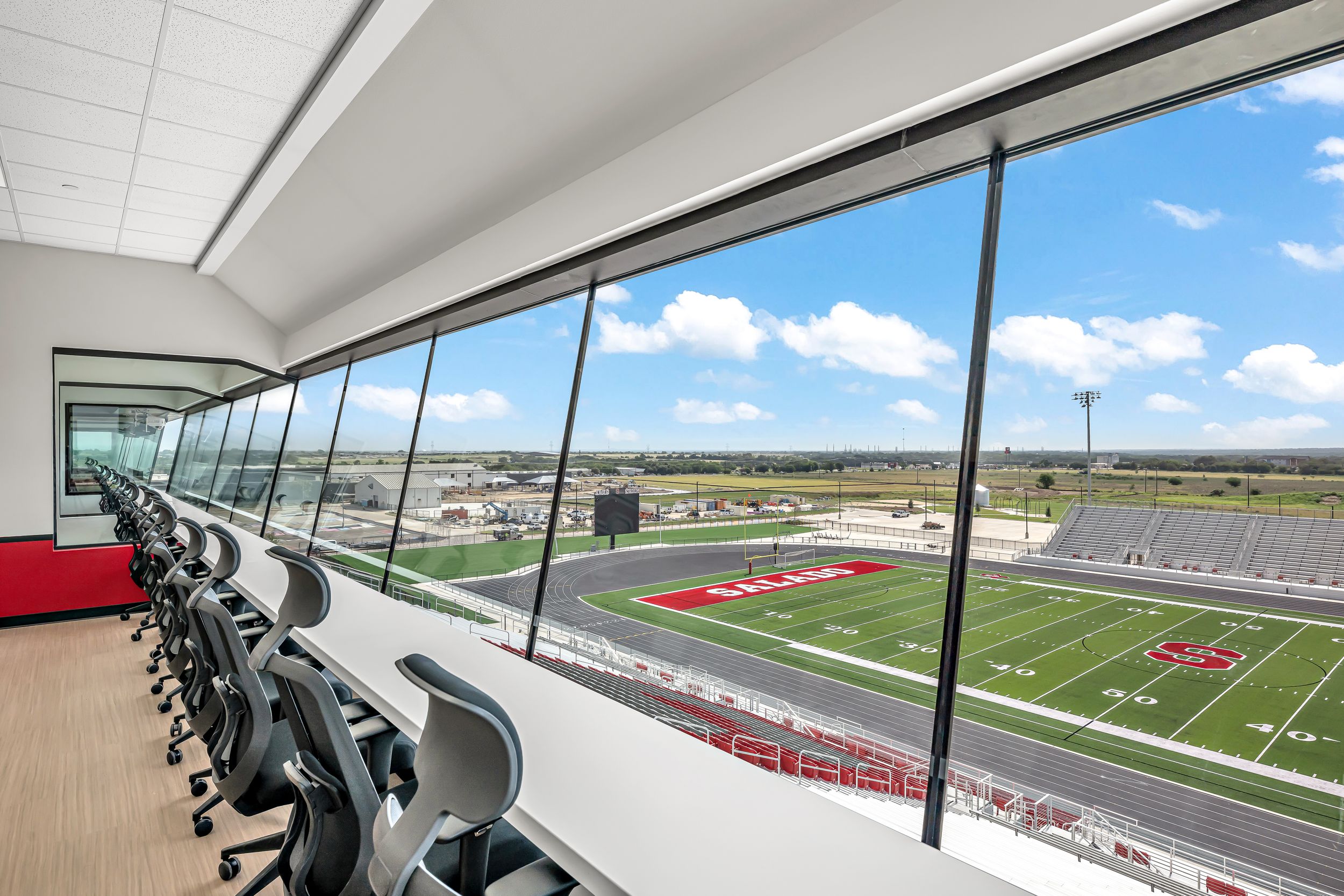 Press box interior with rows of workstations overlooking a red and white football field.