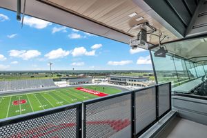 Open-air press box balcony with camera mount overlooking a high school football stadium.