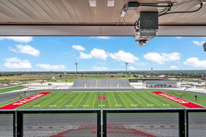 Elevated press box view of a red-painted high school football field on a sunny day.