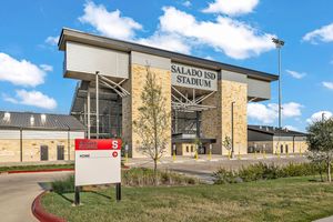 Exterior view of Salado ISD Stadium featuring limestone facade, modern architecture, and a sign near the entrance on a sunny day.