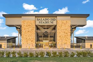 Exterior view of Salado ISD Stadium featuring a modern tan brick facade with large signage under a blue sky.