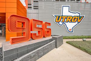 Orange 956 area code sculpture displayed outside UTRGV stadium with school logo on gray wall.