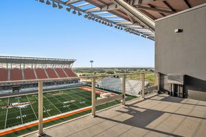 Elevated stadium balcony overlooking the Vaqueros football field with orange seating and open blue sky views.