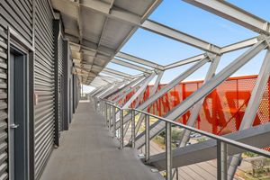 Modern stadium corridor with steel railings, metal roof structure, and vibrant orange perforated panels along walkway.