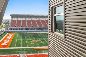 Aerial view of Vaqueros football stadium green turf and orange stands from a modern corrugated metal structure.