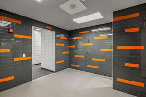 Modern team shower room with gray and orange tile accents, multiple shower heads, and skylight ceiling panel.