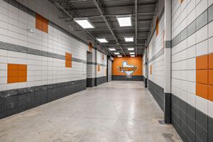 Wide stadium tunnel corridor featuring Vaqueros team logo, orange and white tile walls, and concrete flooring.