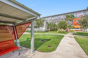 Outdoor walkway and bus shelter near Robert & Janet Vackar Stadium with lush green lawn.
