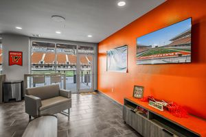 Modern stadium suite lounge with orange accent wall, seating area, and field view.