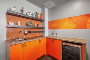Compact stadium suite kitchenette with orange cabinets, mini fridge, and open shelving.