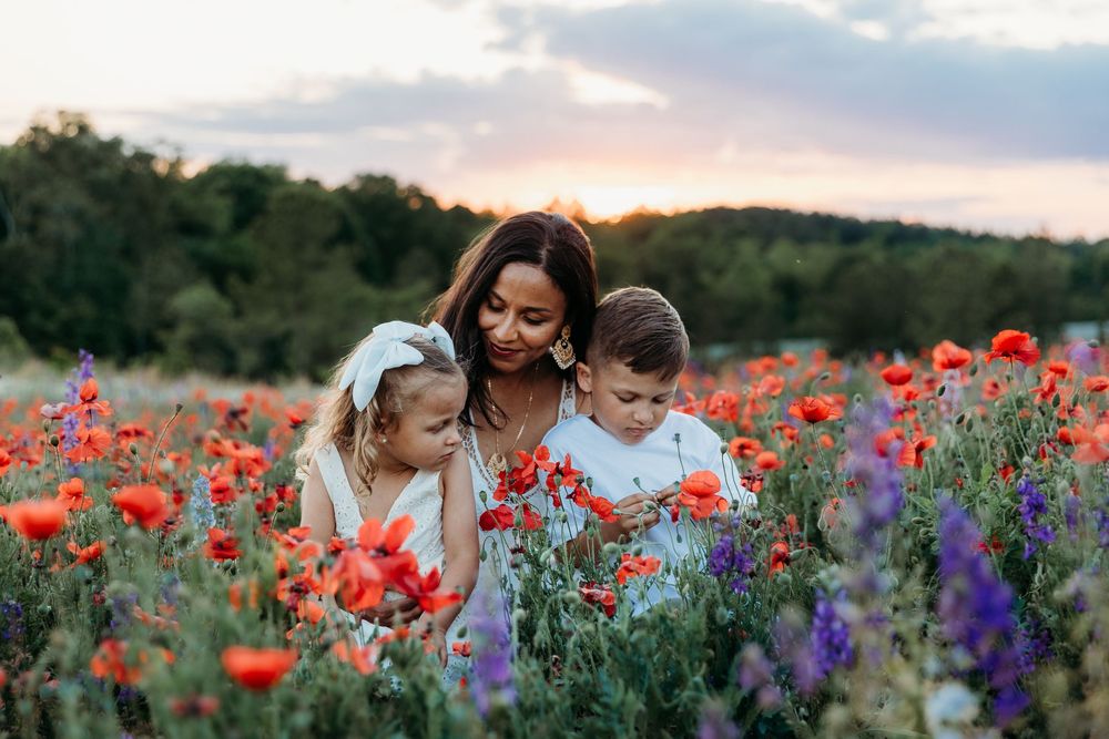 Mother and two children enjoying a vibrant poppy field at sunset, surrounded by red and purple wildflowers.