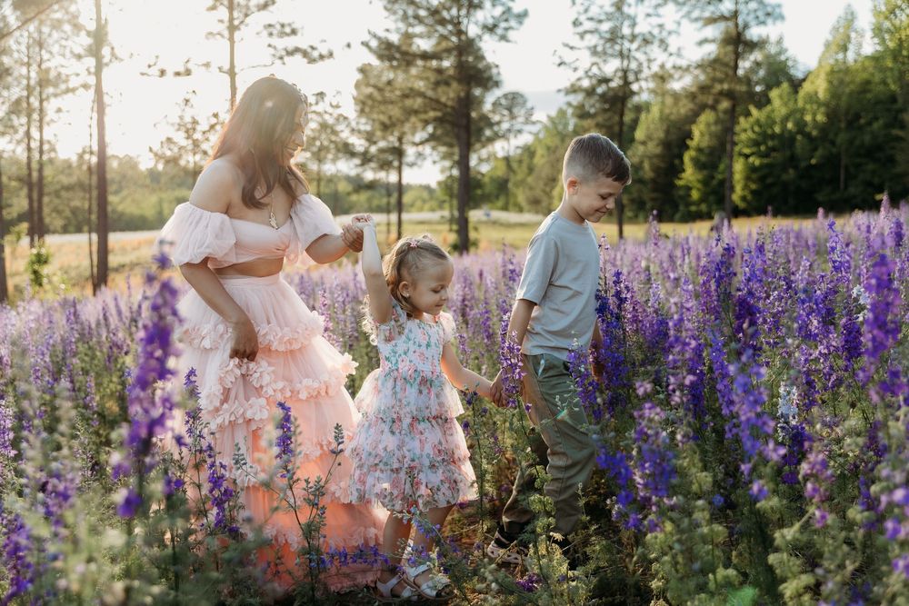 Pregnant woman in pink dress with two children in purple lupine flower field at golden hour sunset.