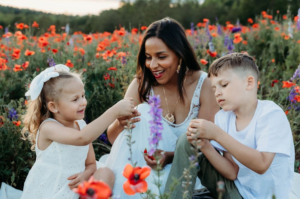 A mother and two children joyfully picking wildflowers in a vibrant poppy field at sunset.