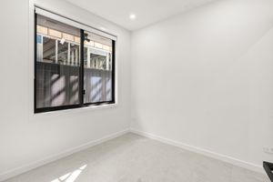 Minimalist empty room with black-framed sliding window, white walls, and light grey polished tile flooring.
