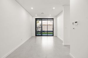 Bright empty room with polished concrete floors, recessed lighting, sliding glass door opening to green courtyard.
