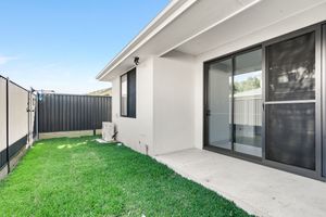 Modern home backyard with lush green lawn, concrete patio, sliding glass doors, and dark privacy fence under blue sky.