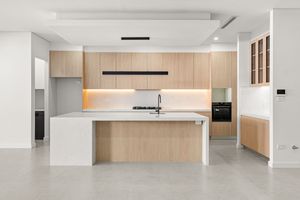 Contemporary kitchen with timber cabinetry, white island bench, black appliances, and concrete-look flooring in open plan layout.