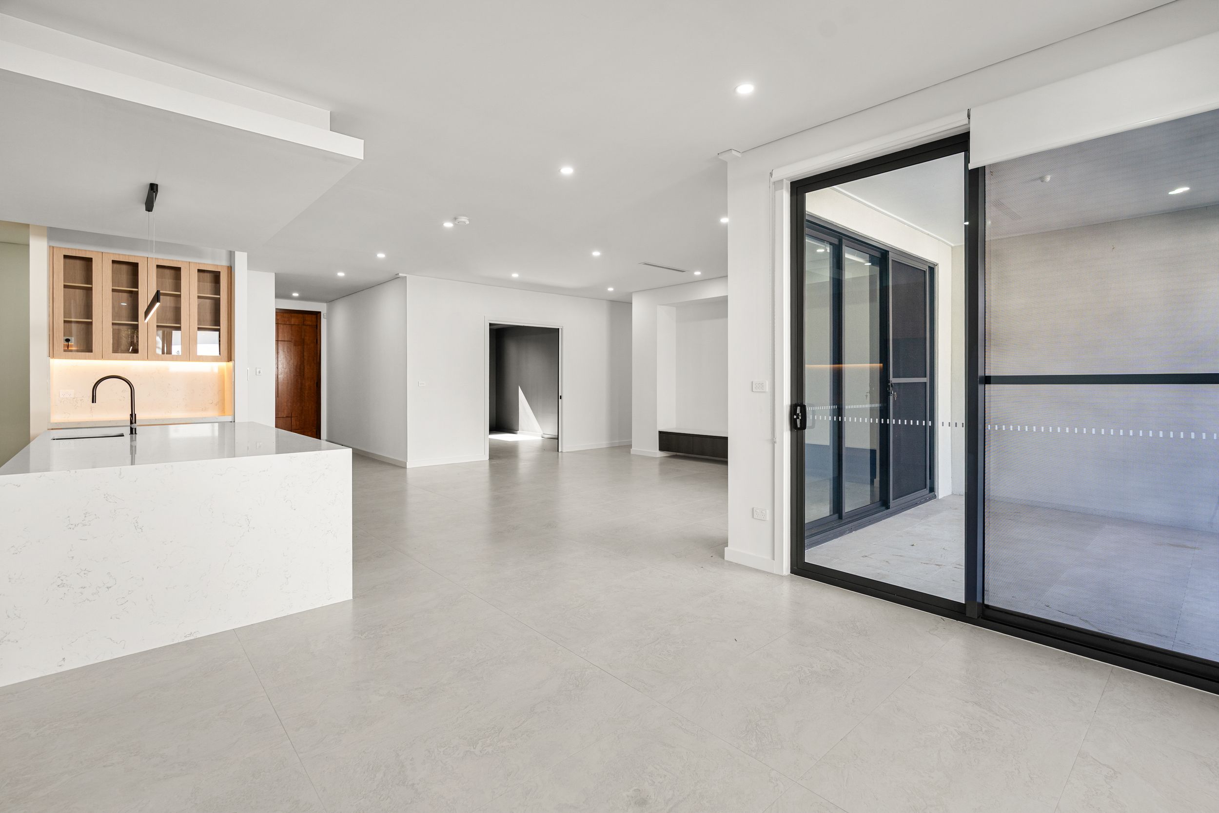 Expansive open plan living area with polished concrete floors, marble island bench, and glass sliding doors.