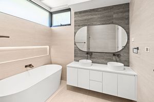 Luxurious bathroom featuring freestanding soaking tub, dual vessel sinks, oval mirror, and elegant grey stone feature wall tiles.