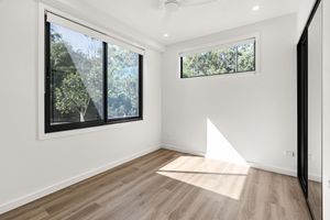 Bright empty bedroom with black-framed windows overlooking lush green trees and timber hardwood flooring.