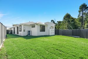 Modern white rendered home exterior with lush green lawn, fenced backyard, and mature trees in background.