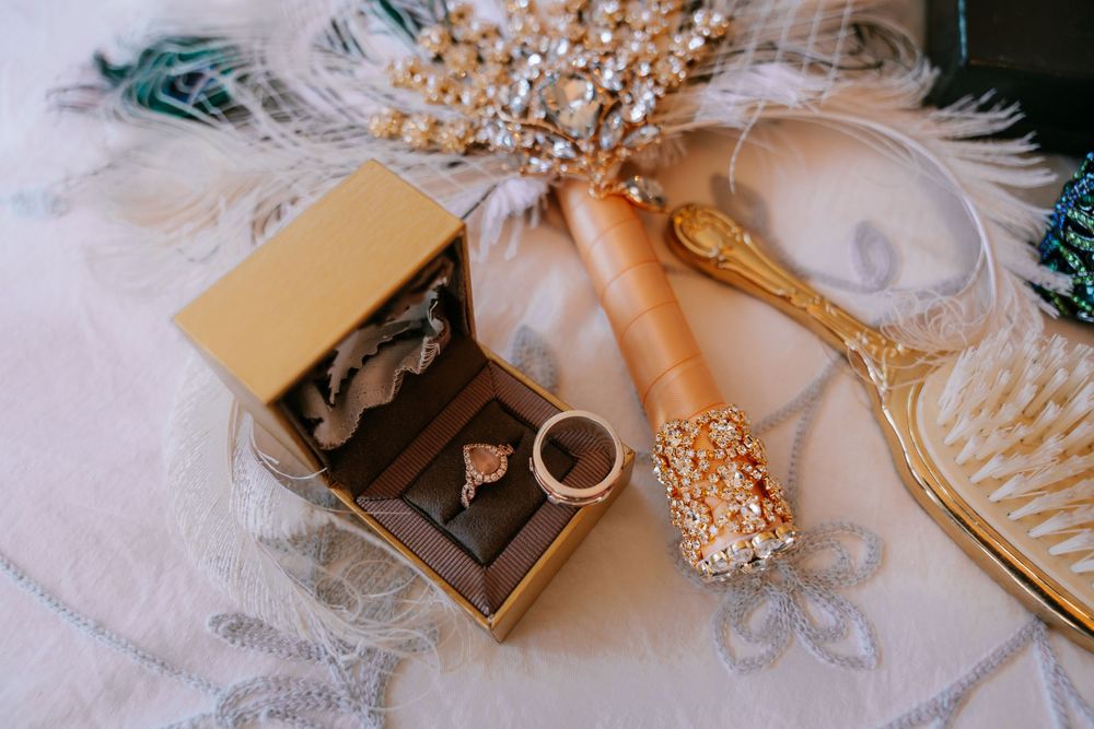 Gold jewelry box with rings, vintage hair comb, and ornate brush on lace fabric with feather decor.