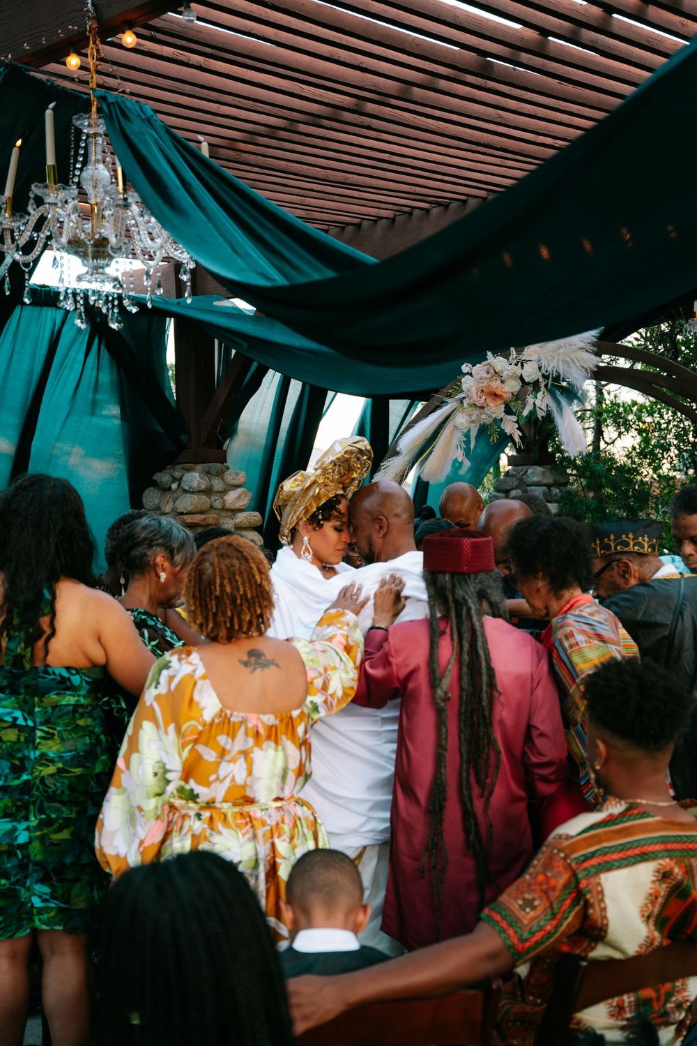 Guests gather under teal draped canopy with chandelier at an elegant outdoor cultural wedding ceremony.